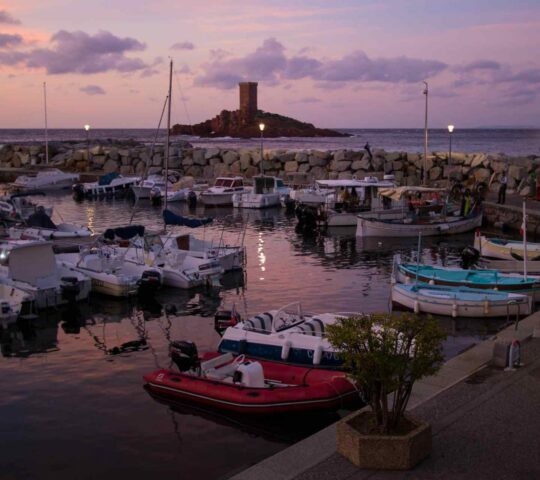 A small harbour in the French town of Saint-Raphael at sunset with a rocky outlet with stone tower in the background