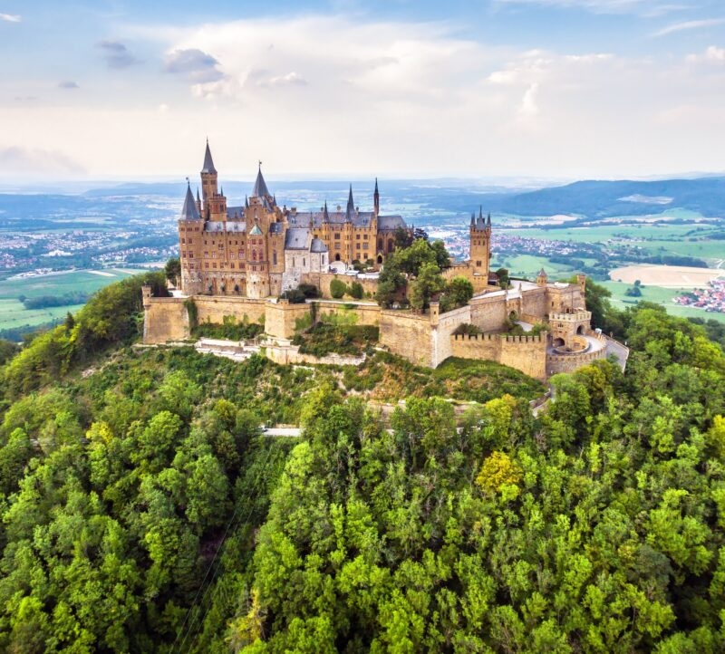Aerial view of the historic Hohenzollern Castle surrounded by dense green forest on a hilltop.