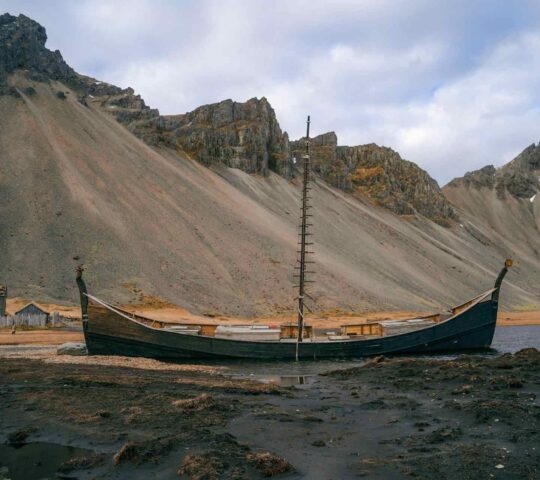 A replica Viking long boat abandoned on a black sand beach in Iceland