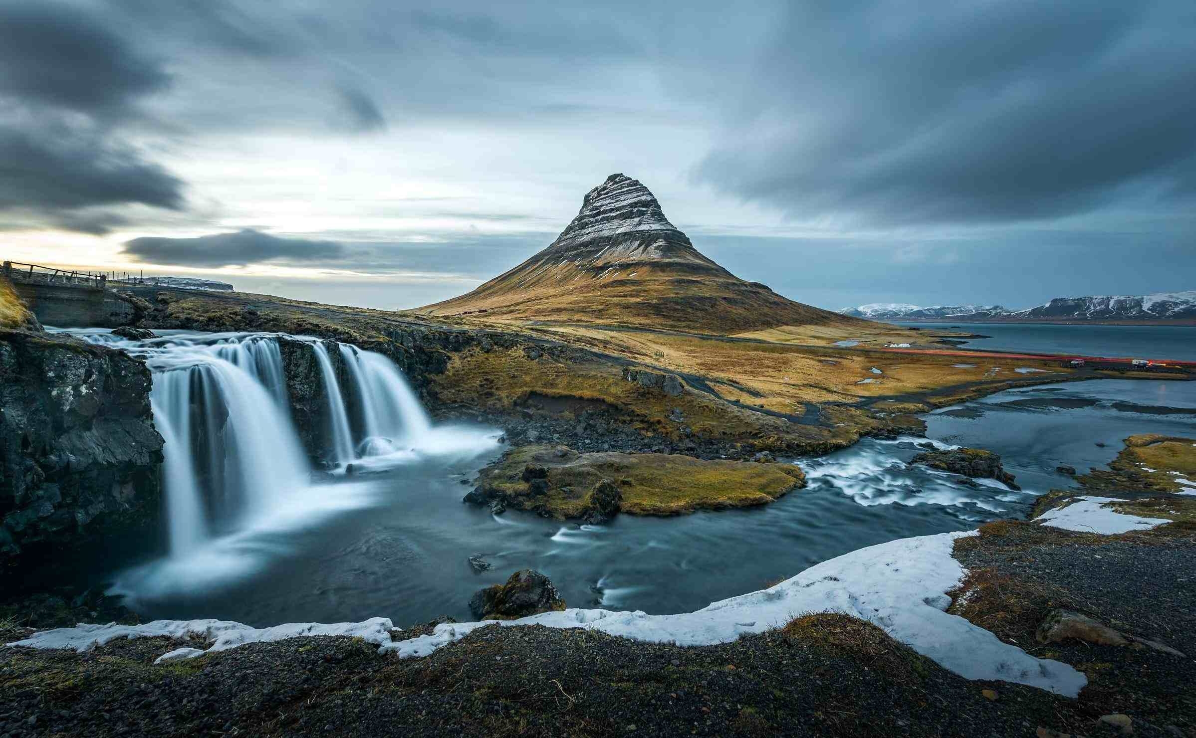 Waterfalls flowing into a dark blue pool with a green hill in the background in Iceland