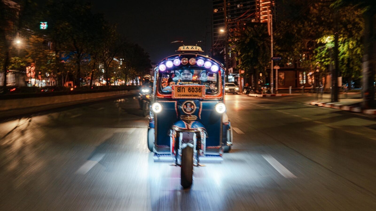 A Bangkok tuk tuk with bright lights on an empty evening road.