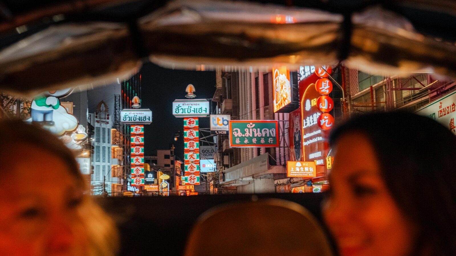 Bangkok's Chinatown brightly lit and colourful street signs with a mother and daughter in the foreground enjoying a private tuk tuk ride.