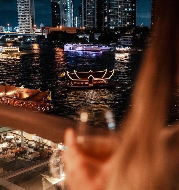 View of Chao Praya river in Bangkok as a woman looks on with a drink from her balcony.