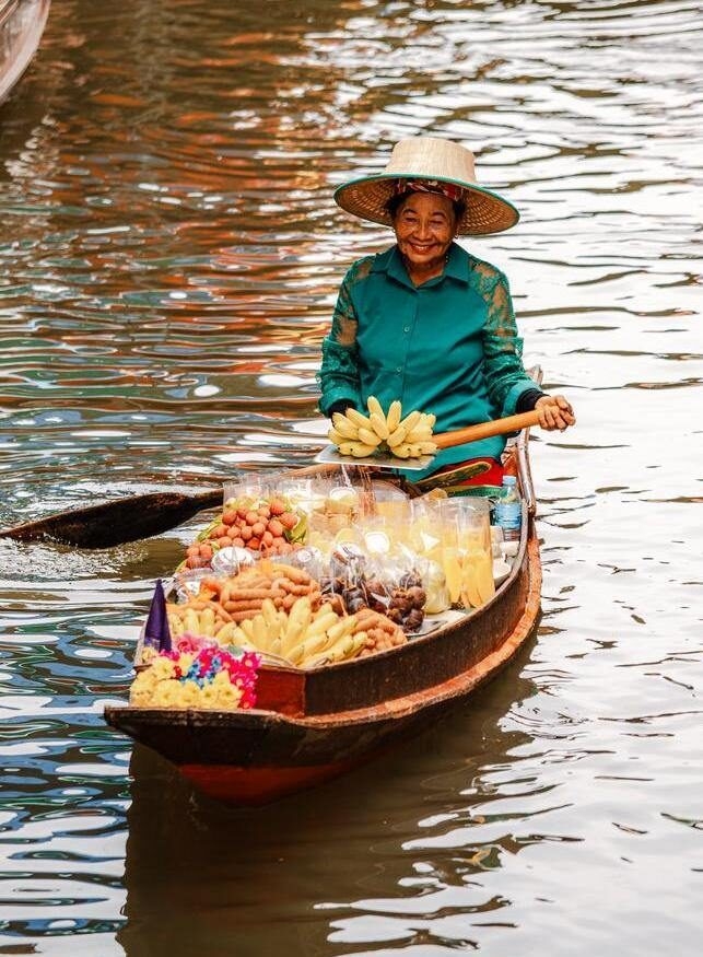 A woman selling fruit smiles on her boat at a floating market in Thailand.