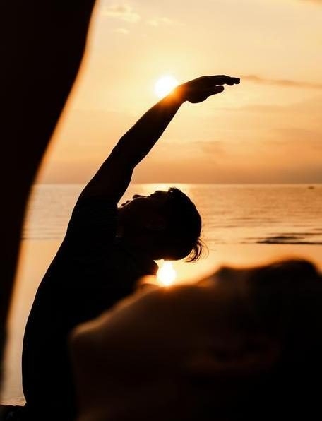 A private sunrise yoga experience as a yoga teacher raises their arm in the sunlight.