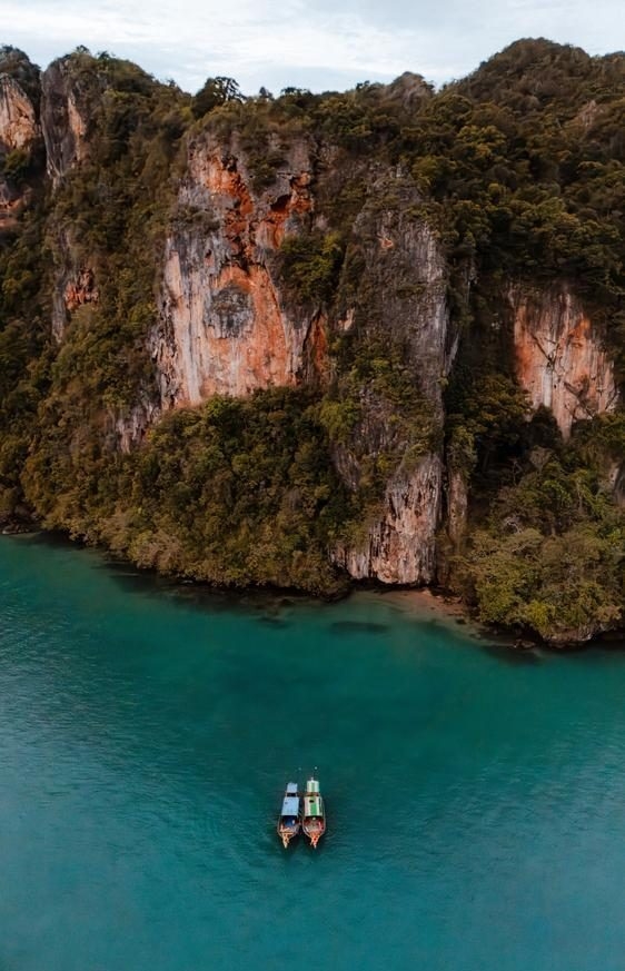 An aerial view of two long tail boats in front of limestone cliffs and turquoise ocean