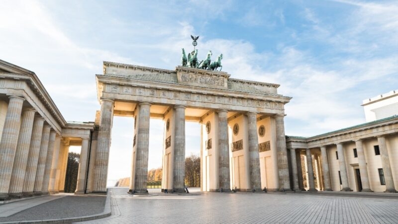 The Brandenburg Gate monument featuring tall stone columns and a horse-drawn chariot statue against a blue sky.