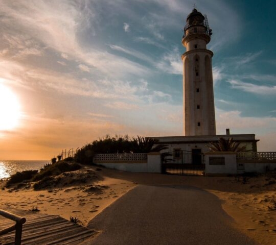 A lighthouse on sandy dunes at sunset near the ocean, a popular location for cape trafalgar riding.