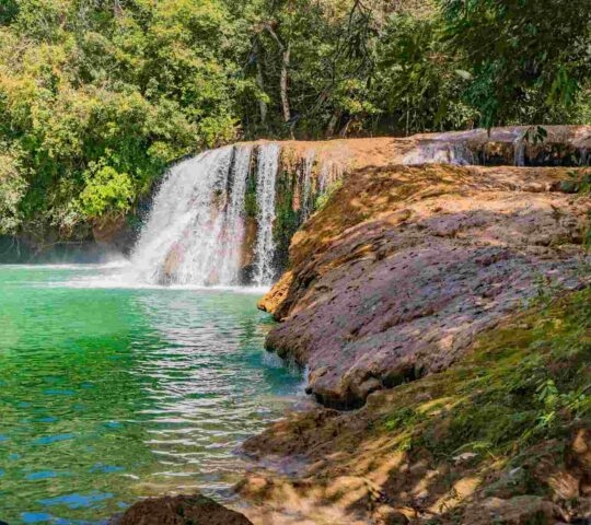 A small waterfall pouring into a green pool surrounded by rocks near Estancia Mimosa nature reserve in Bonito