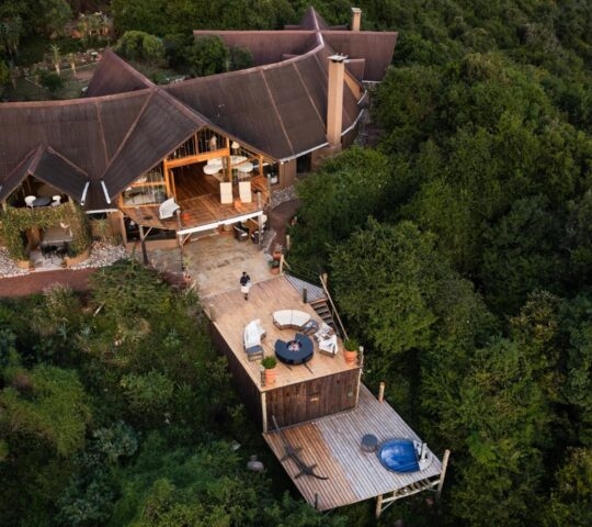 Aerial view of Cottar's Bush Villa, a multi-level lodge with a brown roof and tiered wooden decks amid lush forest.