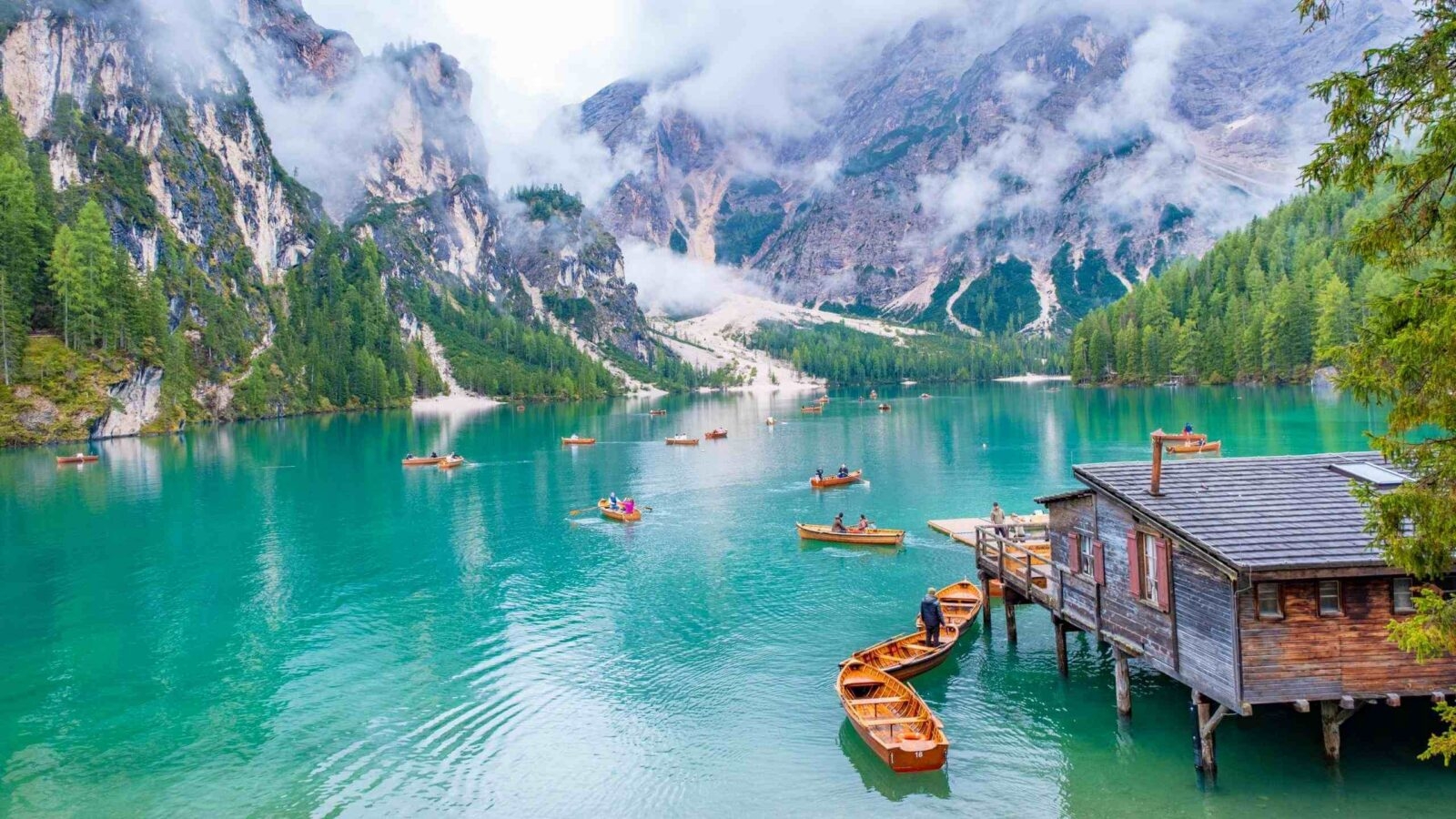 Small boats floating on a turquoise lake surrounded by mountains in the Dolomites