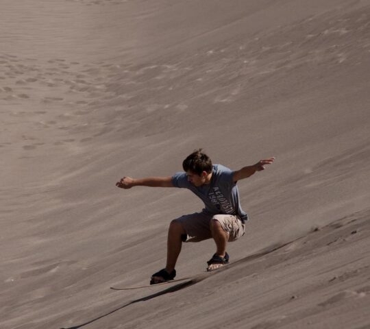 A man sandboarding down a sand dune in the Sahara desert
