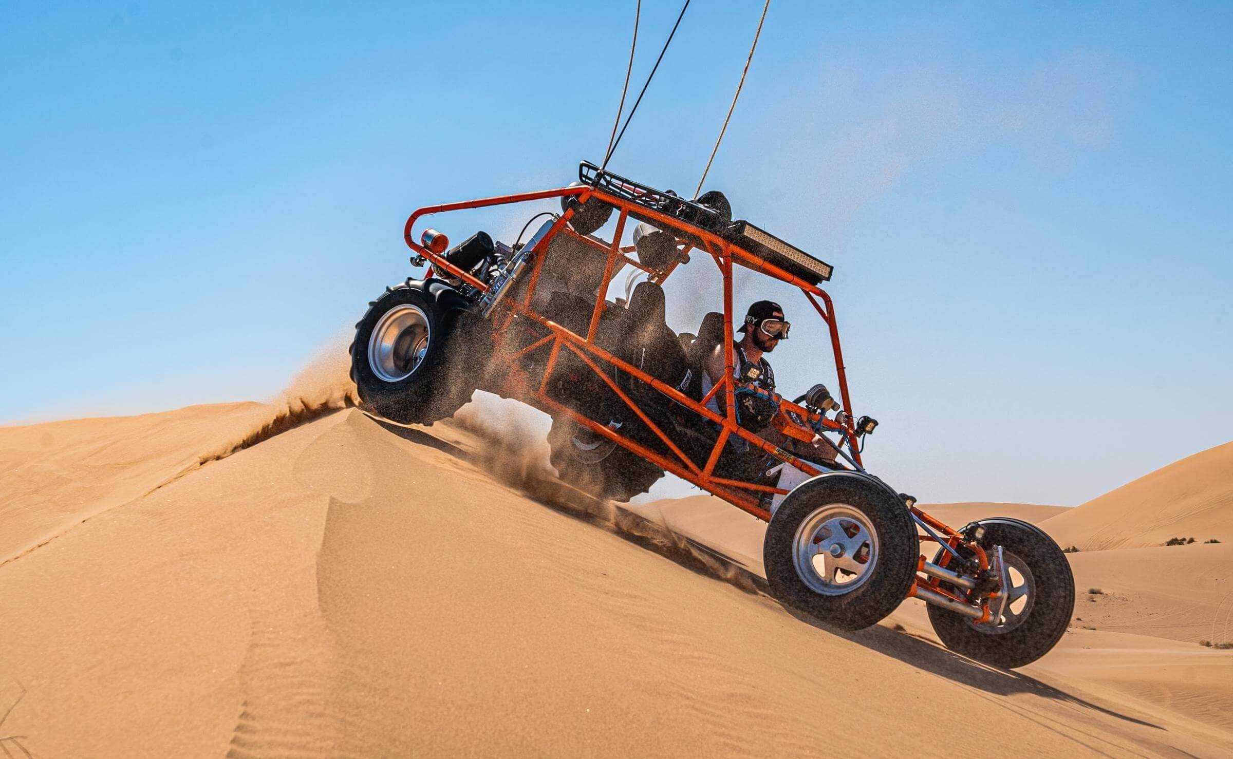 People riding a dune buggy over the peak of a sand dune in the Sahara desert