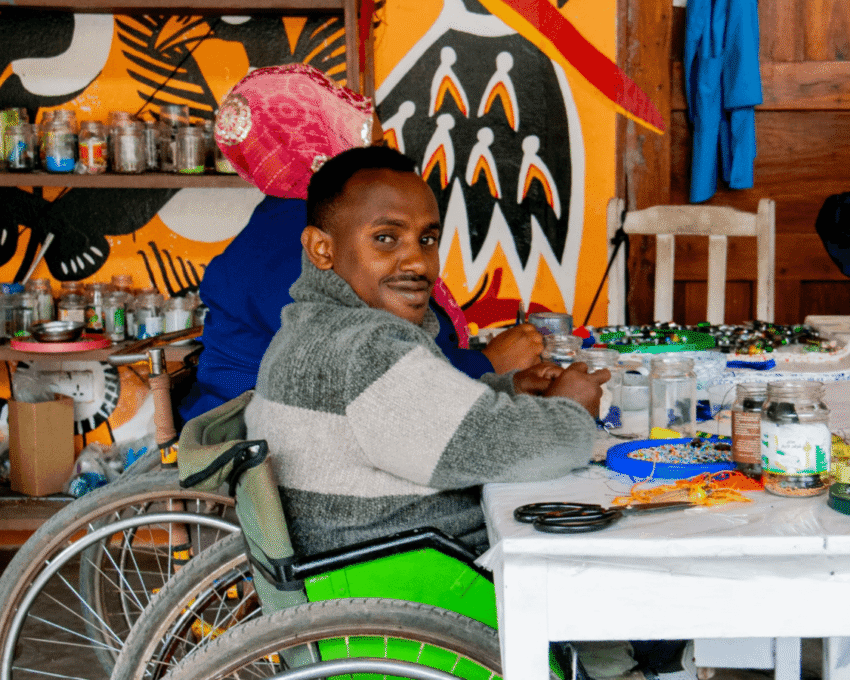 An artist in a wheelchair making jewellery from beads at the Shanga experience in Arusha